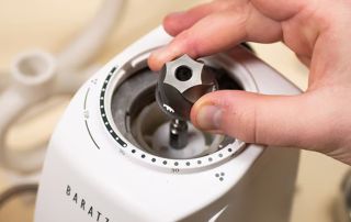 A hand taking the burr out of a Baratza Encore coffee grinder.